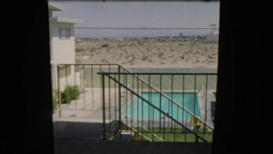 1966 Las Vegas footage frame showing a private pool and swimmer from a shaded balcony, with desert terrain behind the property.