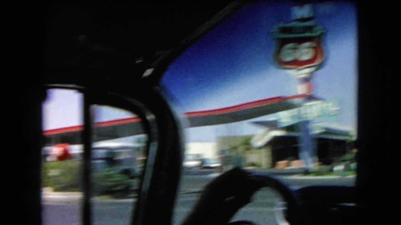 Blurred car-window view of a Route 66-style gas station sign and roadside building.