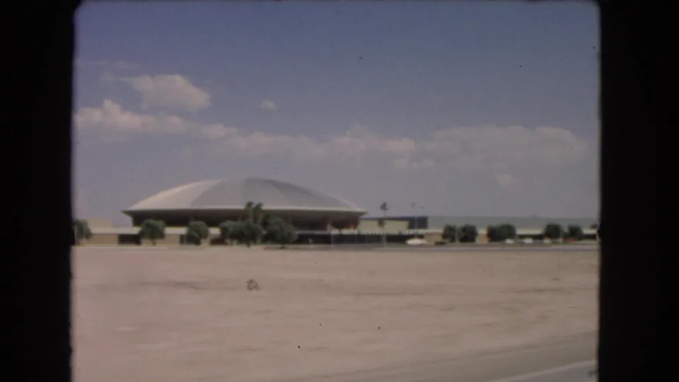 The final frame shows a distant dome-shaped sporting arena across a broad paved area, with low roadside structures, small trees, and car-window framing in 1966 Las Vegas footage.