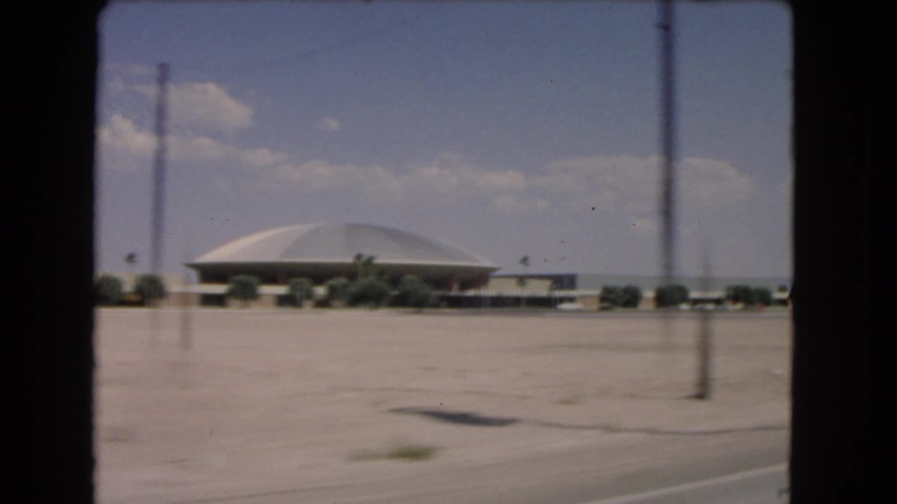 1966 Las Vegas road-trip frame showing a low domed building beyond desert roadside and sparse vegetation.