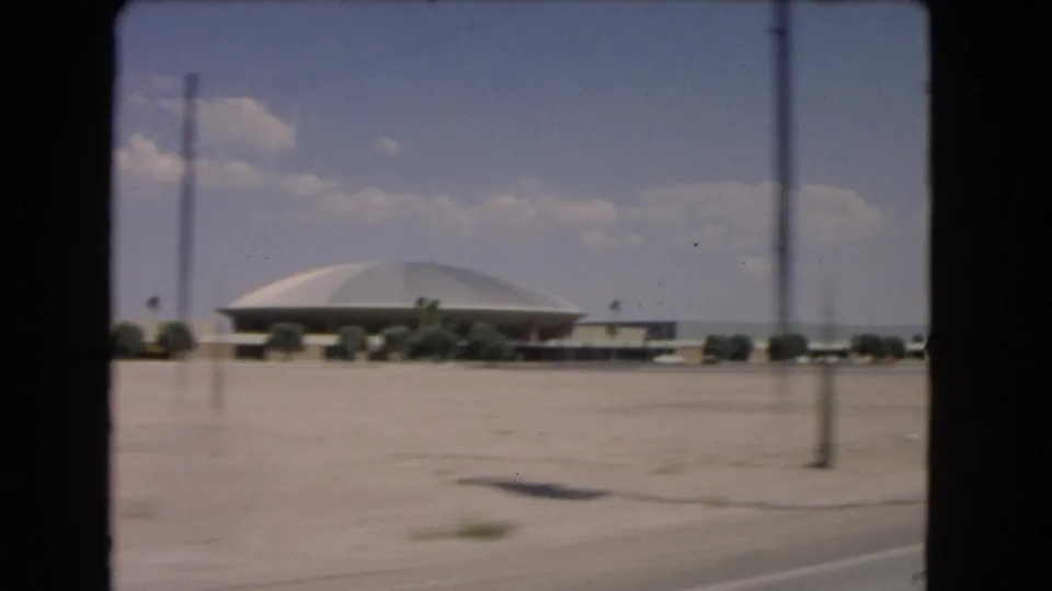 1966 Las Vegas road-trip frame showing a low domed building beyond desert roadside and sparse vegetation.