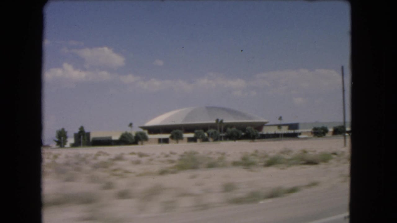 1966 Las Vegas desert approach with a domed building, roadside scrub, and soft 8mm motion blur.