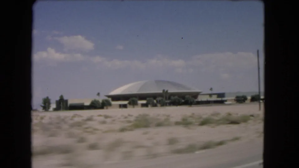 1966 Las Vegas desert approach with a domed building, roadside scrub, and soft 8mm motion blur.