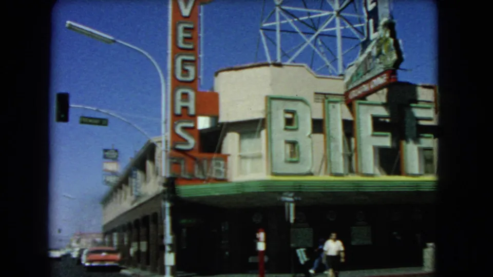 1966 Las Vegas 8mm frame with Biff's Club facade, Las Vegas Club vertical sign, a traffic signal, cars, and sidewalk pedestrians.