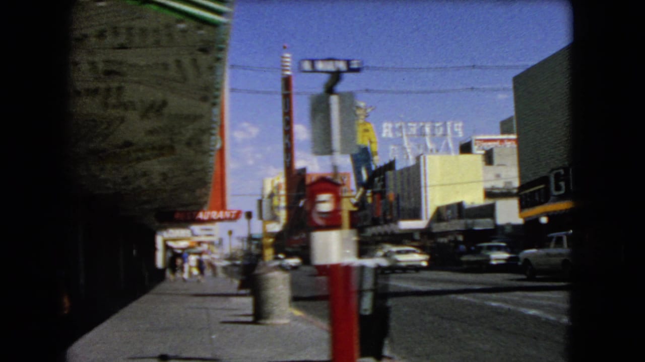 Sidewalk and roadway beside large casino signs and parked or passing cars.