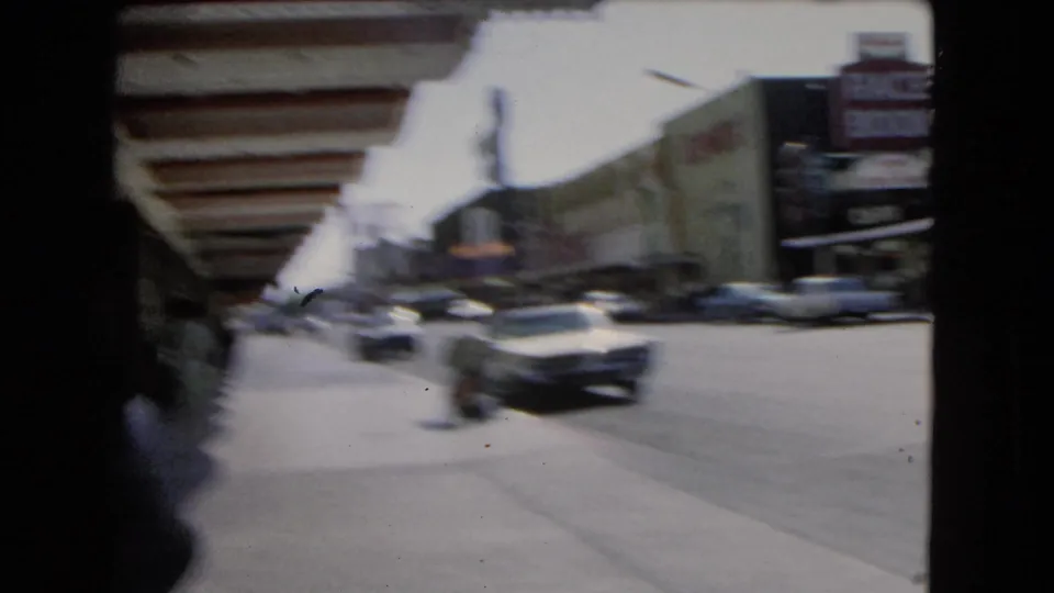 Motion-blurred 1966 Las Vegas downtown view with passing cars, sidewalk pedestrians, and commercial signs.