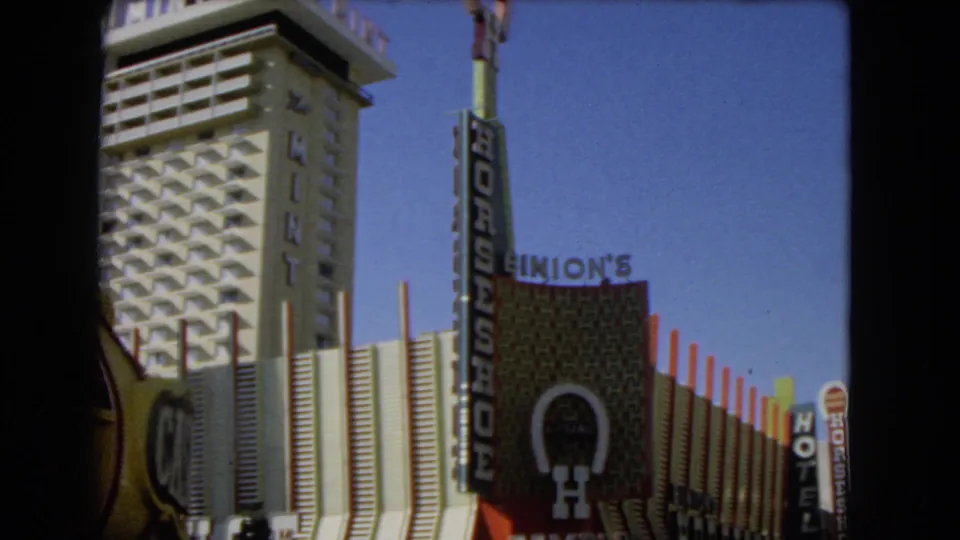 1966 Las Vegas home-movie frame with low-angle casino signage including The Mint, Horseshoe, Binion's, and a hotel sign.
