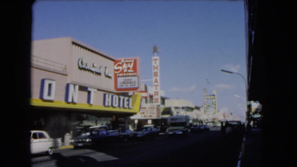1966 Las Vegas street frame with large Mint Hotel letters, Skyline Theatre signage, cars, storefronts, and sunlit roadway.