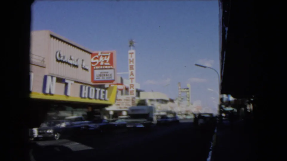 1966 Las Vegas street view framed by shadow, with Mint Hotel signage, theatre sign, moving cars, and commercial buildings.