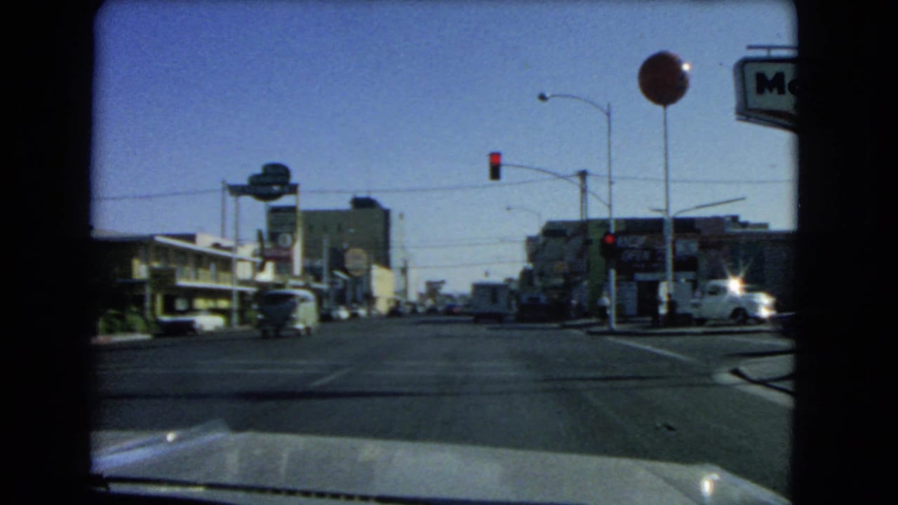 Intersection seen through a windshield with red traffic light, road signs, cars, and motel-style buildings.