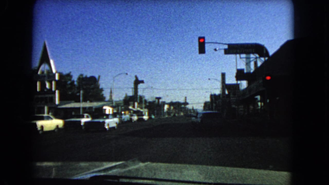 View through a windshield toward a Las Vegas street with classic cars stopped at a red light.