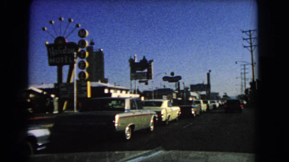1966 Las Vegas roadside scene showing classic cars, a visible Holiday Motel sign, other motel signage, utility poles, and 8mm vignette edges.