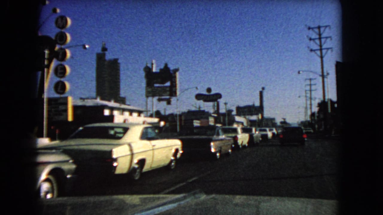 1966 Las Vegas street view from a moving vehicle, with mid-century cars passing motel and hotel-style signs under a clear sky.