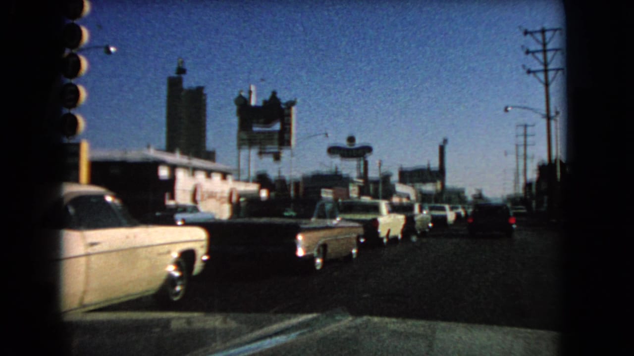 Las Vegas traffic scene from 1966, showing classic cars, a vertical motel sign, roadside buildings, and power poles.