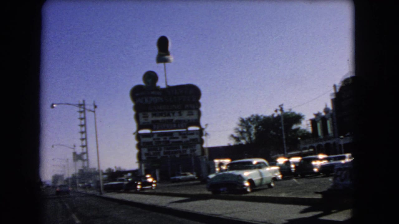 1966 Las Vegas street view from a moving car, with a tall gambling hall and restaurant sign, traffic, sidewalk, and streetlights.