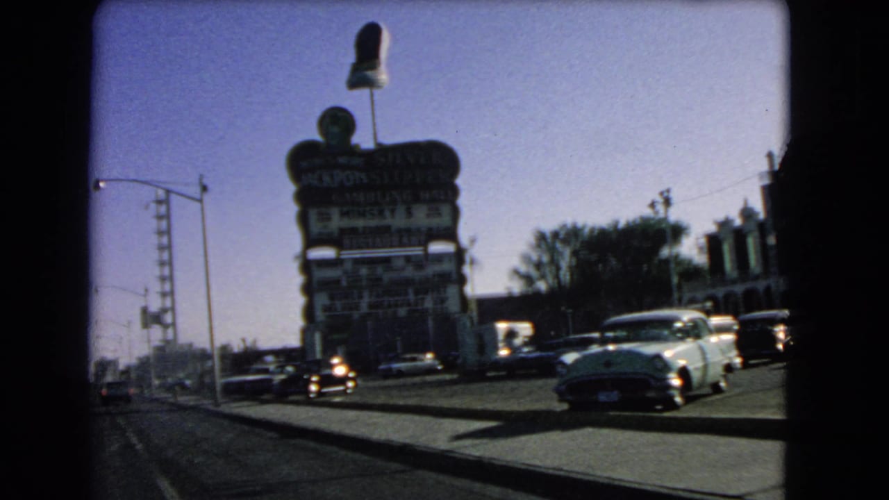Cars pass a tall commercial sign along a broad city street under a clear sky.