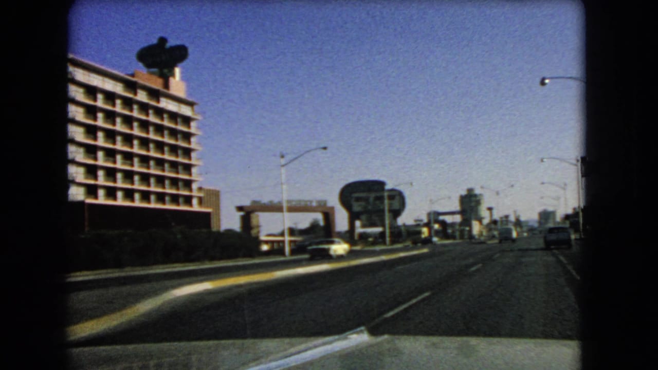 Moving road view with a large building on the left, lane markings, cars, and prominent roadside signs ahead.