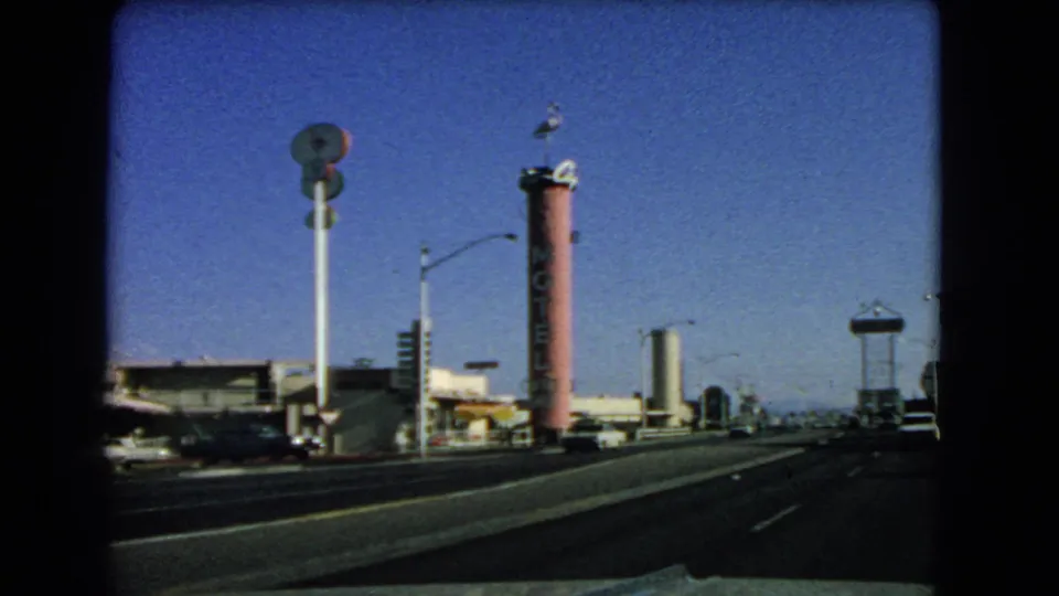 1966 Las Vegas street scene with broad lanes, a tall pink roadside sign, low commercial buildings, cars, and distant signage.
