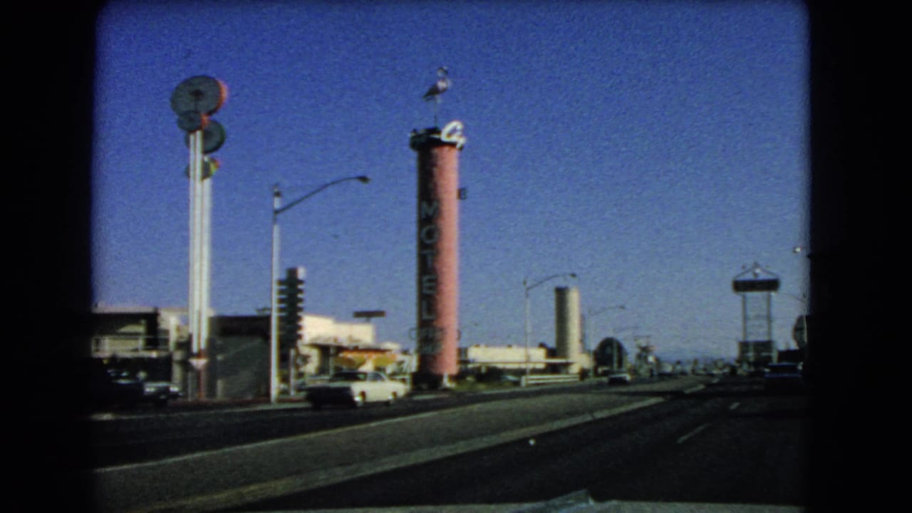 Roadside motel sign and commercial buildings seen from a moving vehicle under clear sky.