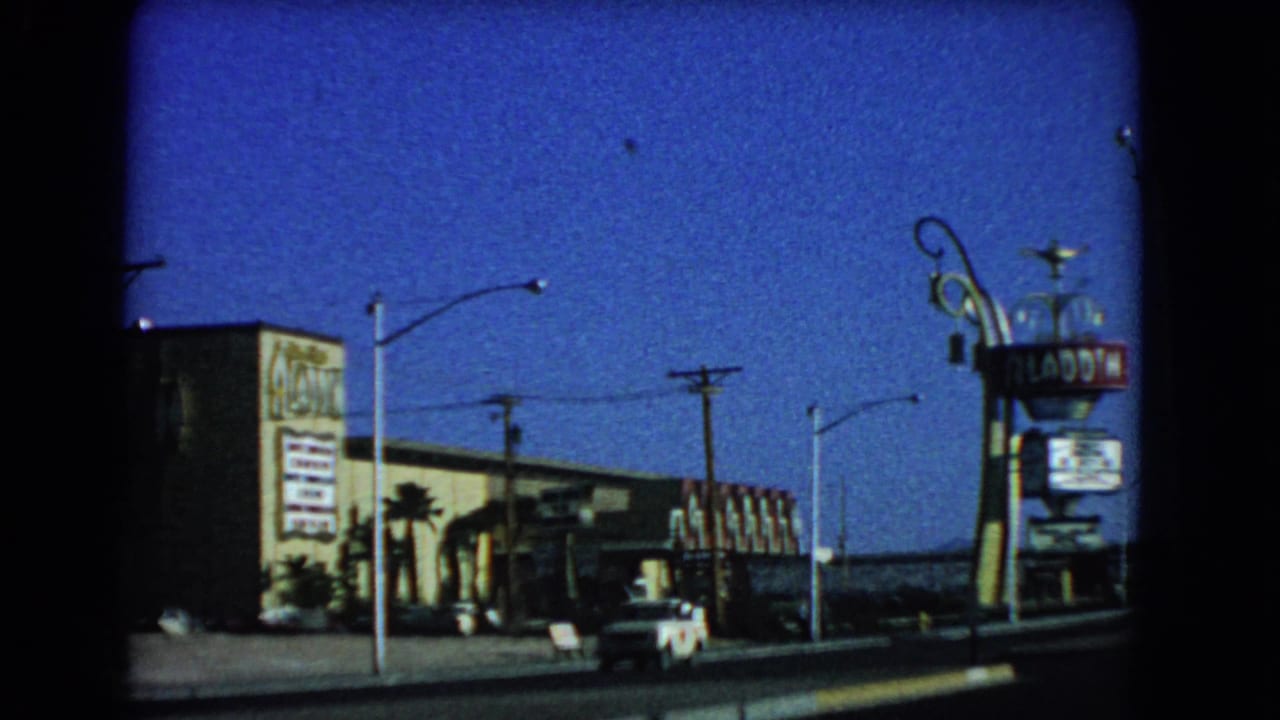 Aladdin Hotel roadside sign beside the hotel exterior and passing cars.