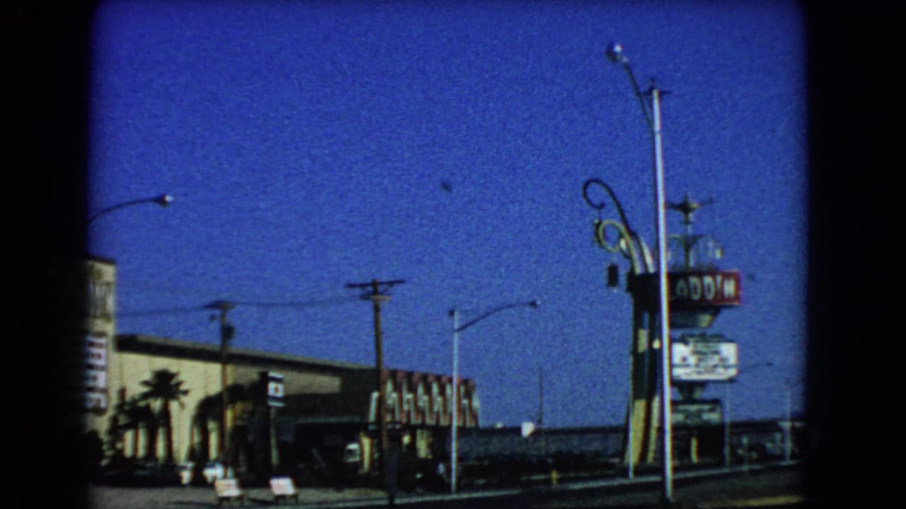 1966 Las Vegas view of the Aladdin Hotel sign and exterior from across the road, with utility poles, streetlights, palms, and open sky.