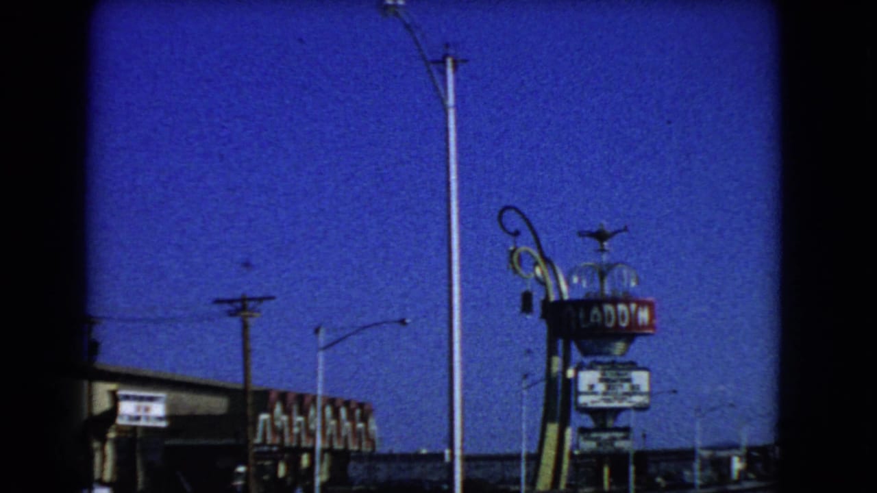 1966 Las Vegas street view with the Aladdin Hotel sign, tall light poles, low commercial buildings, and visible 8mm frame edge.