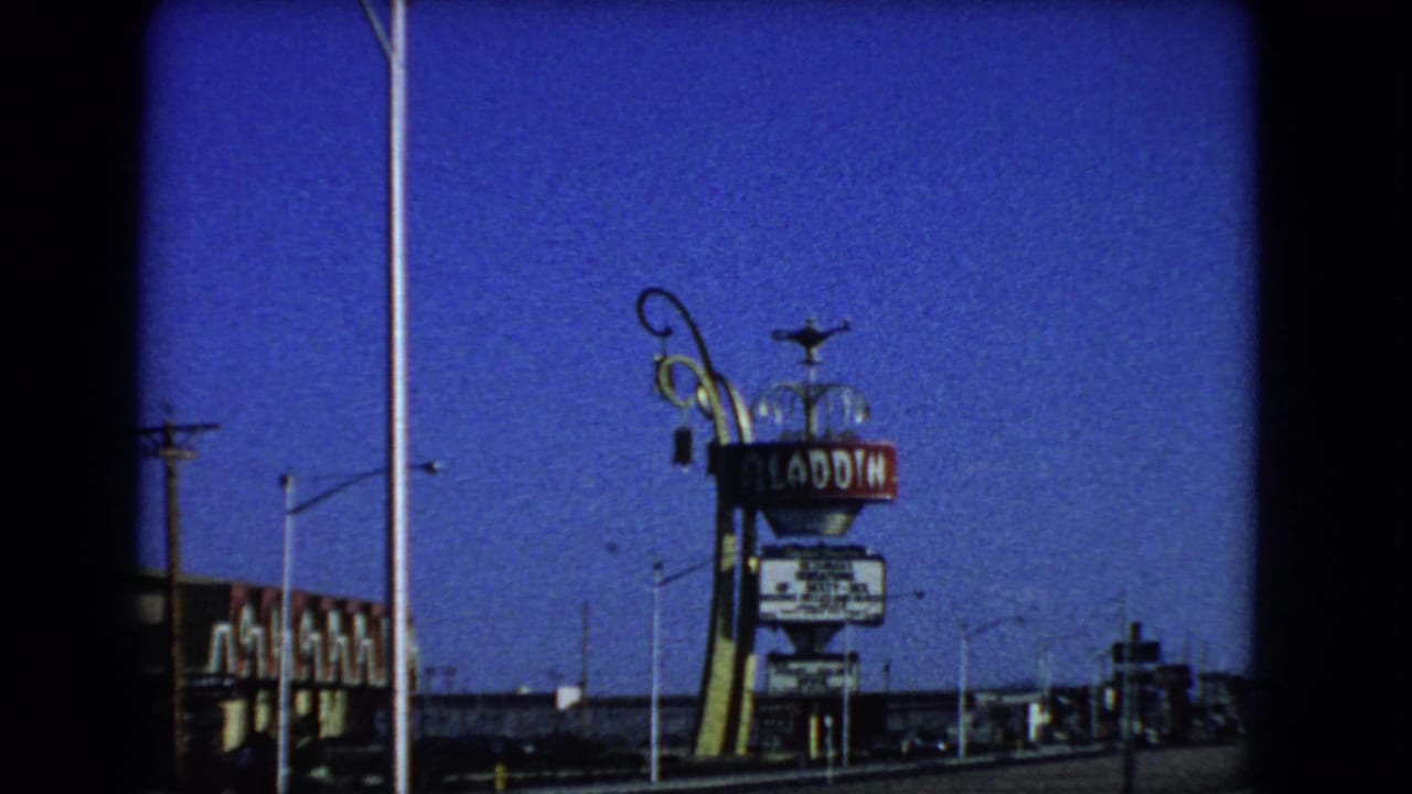 1966 Las Vegas 8mm frame with the Aladdin Hotel sign, decorative sign support, streetlights, utility lines, and low buildings.