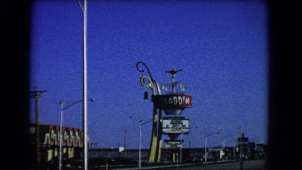 1966 Las Vegas 8mm frame with the Aladdin Hotel sign, decorative sign support, streetlights, utility lines, and low buildings.
