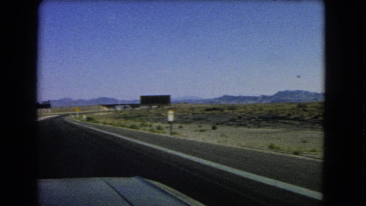 1966 Nevada 8mm road view showing a paved highway through dry desert terrain with low mountains on the horizon.
