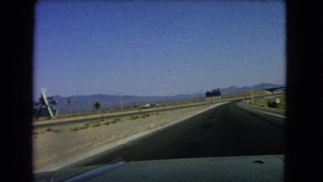 The car passes a distinctive angled roadside structure along a desert highway near Las Vegas in 1966 8mm footage.
