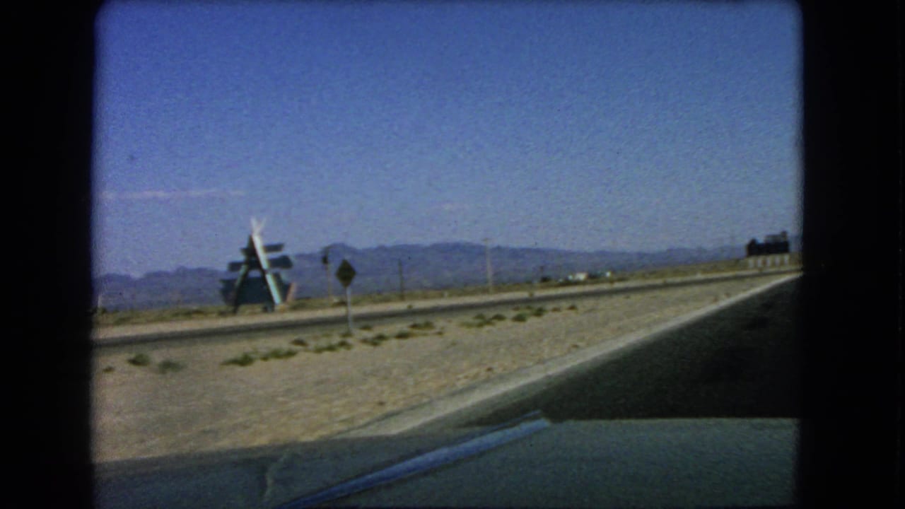 Desert road seen from a car with a large roadside structure and mountains beyond.