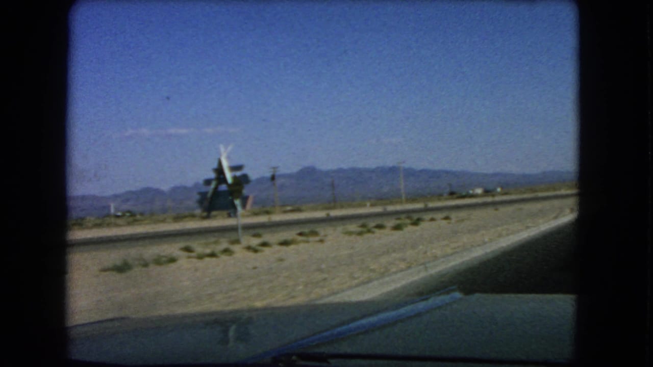 Roadside structure and utility poles beside a desert highway with mountains in the distance.