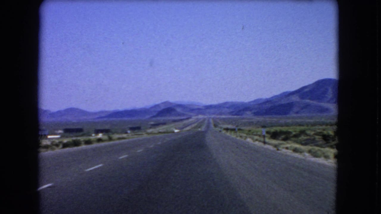 Open road across desert terrain with mountains in the distance.