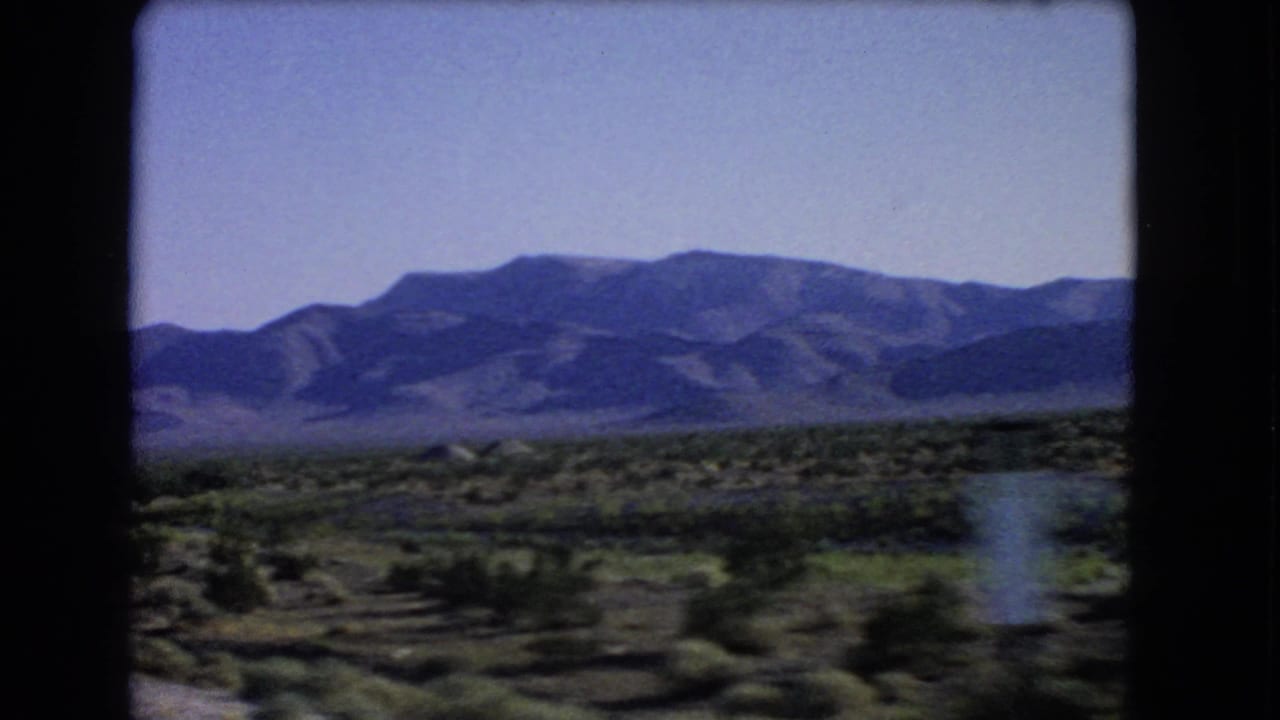 Desert scrub and distant mountains seen from a moving car window.