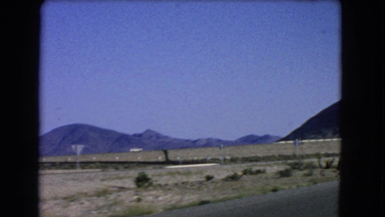 Roadside desert with mountains, pale shoulder, posts, and open sky.