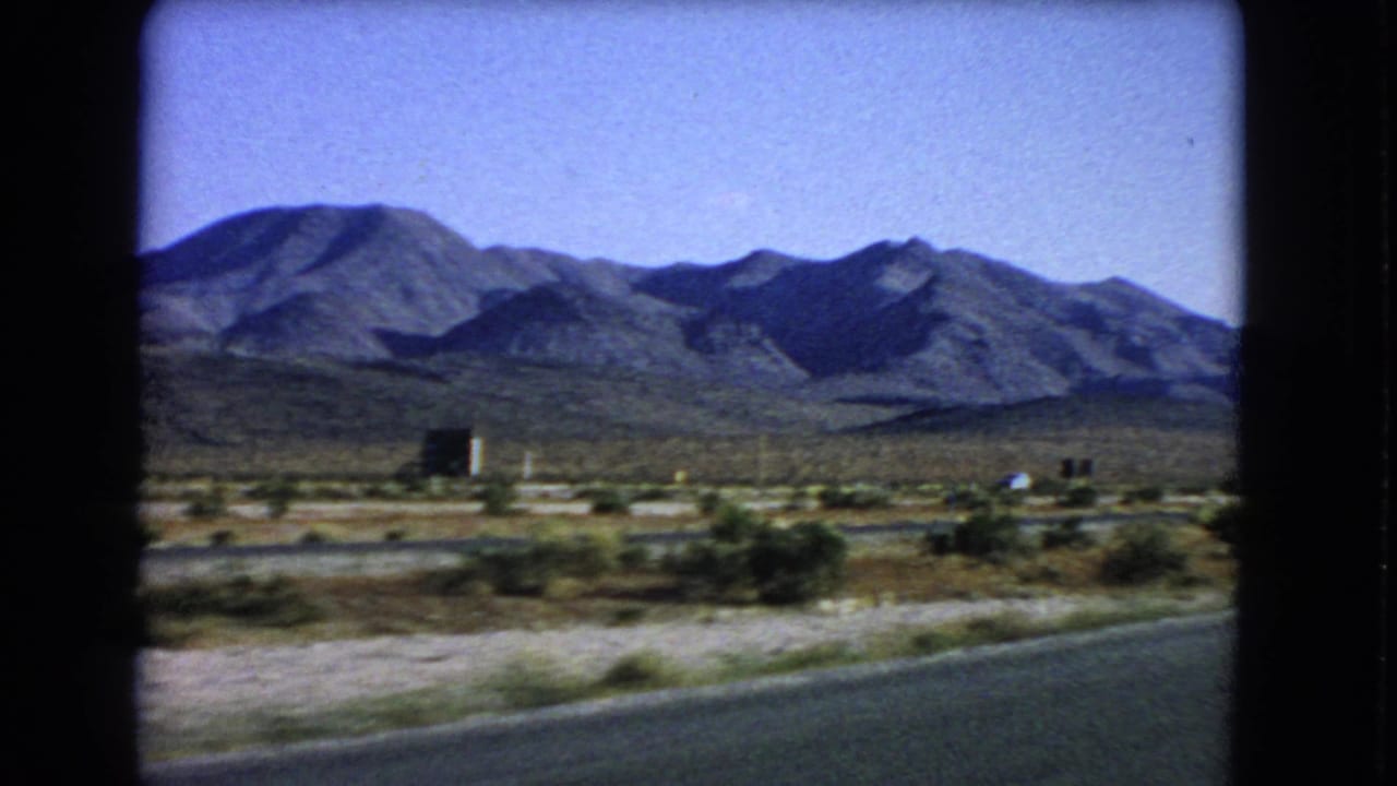 Rugged desert mountains and roadside scrub viewed across a paved road edge.