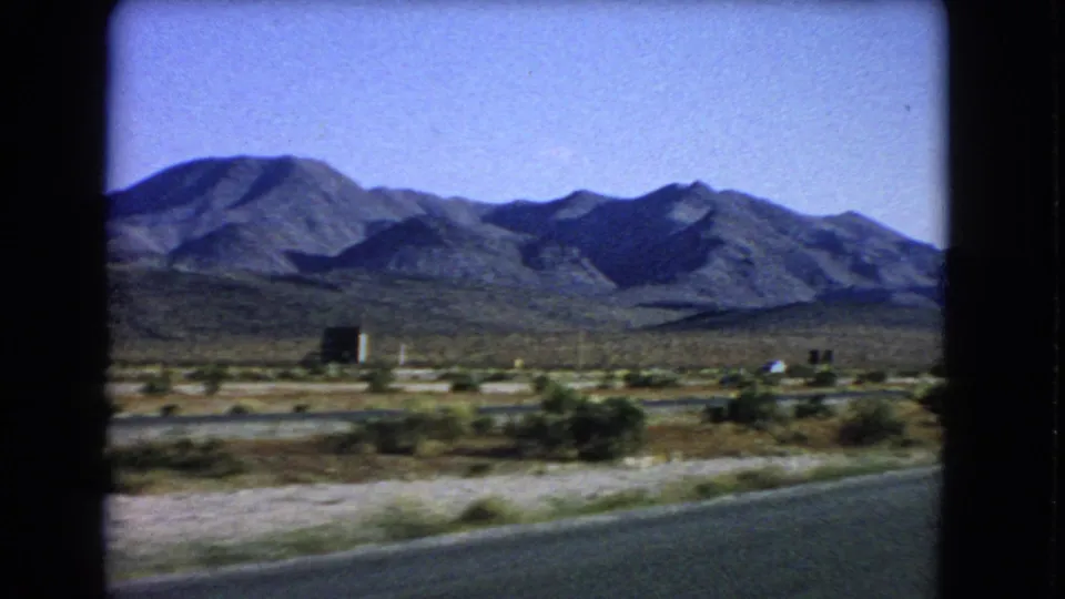 Las Vegas-area 1966 home-movie frame with mountains, desert vegetation, and a roadside foreground from a moving car.
