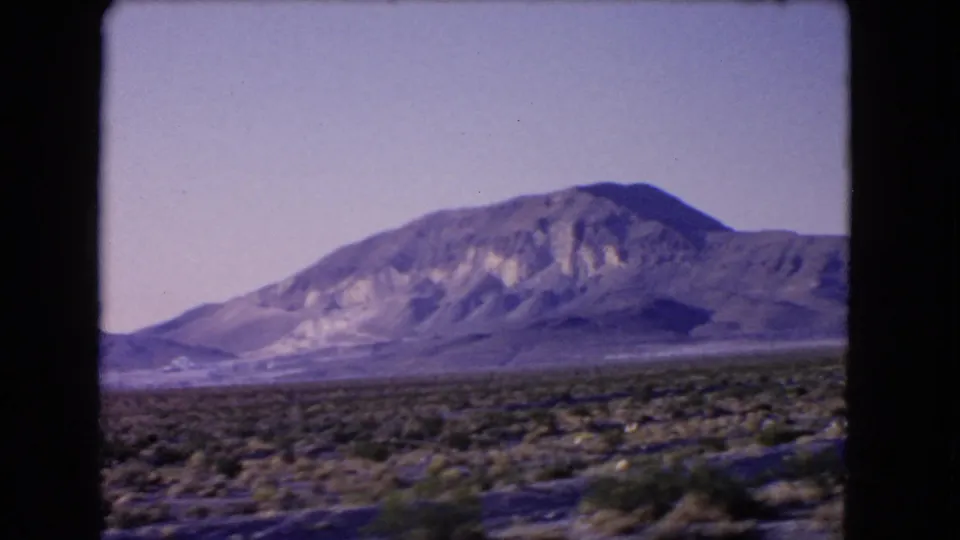 1966 Las Vegas, Nevada 8mm frame showing low desert shrubs and a rugged mountain beyond a broad arid plain.