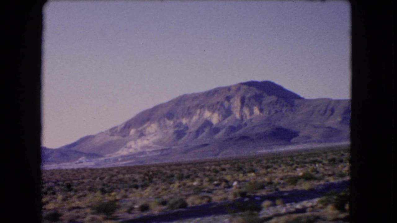1966 Las Vegas, Nevada frame showing roadside desert scrub, a distant rocky mountain, and purplish faded 8mm tones.