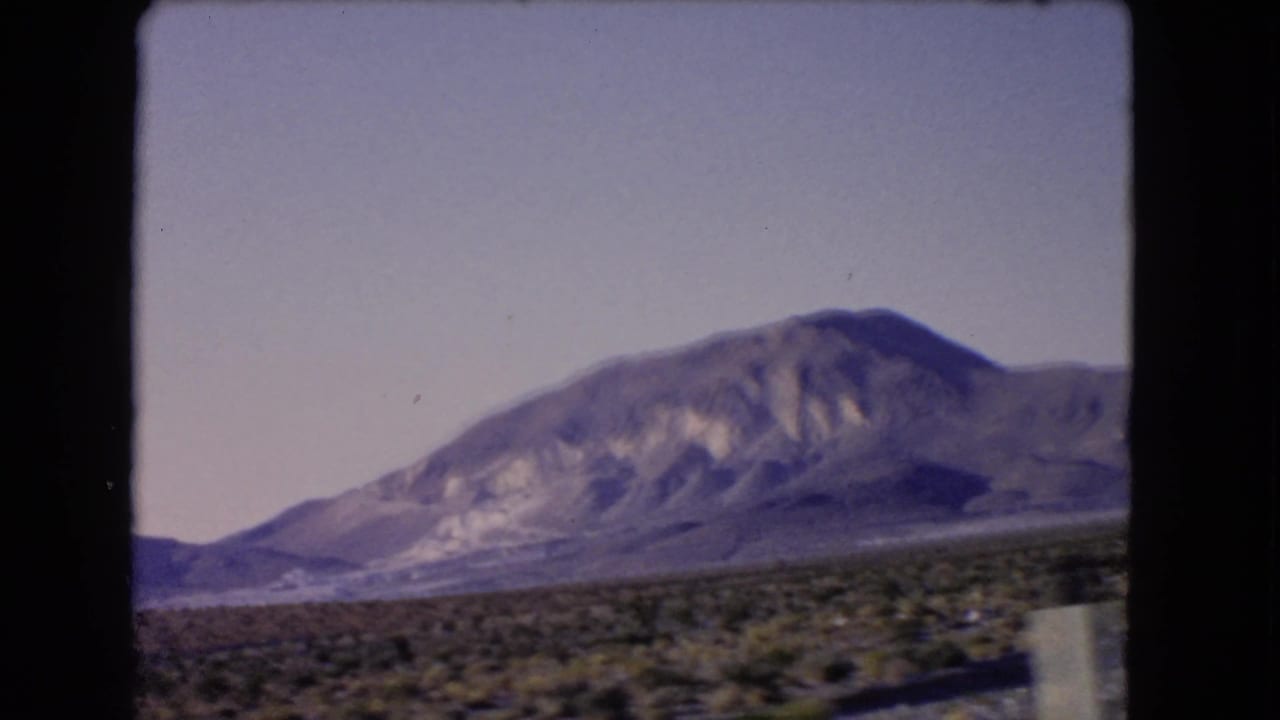 1966 Nevada home-movie view of a mountain range beyond scrub desert, framed by dark 8mm film borders from a moving vehicle.