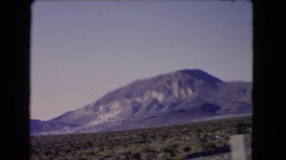 1966 Nevada home-movie view of a mountain range beyond scrub desert, framed by dark 8mm film borders from a moving vehicle.