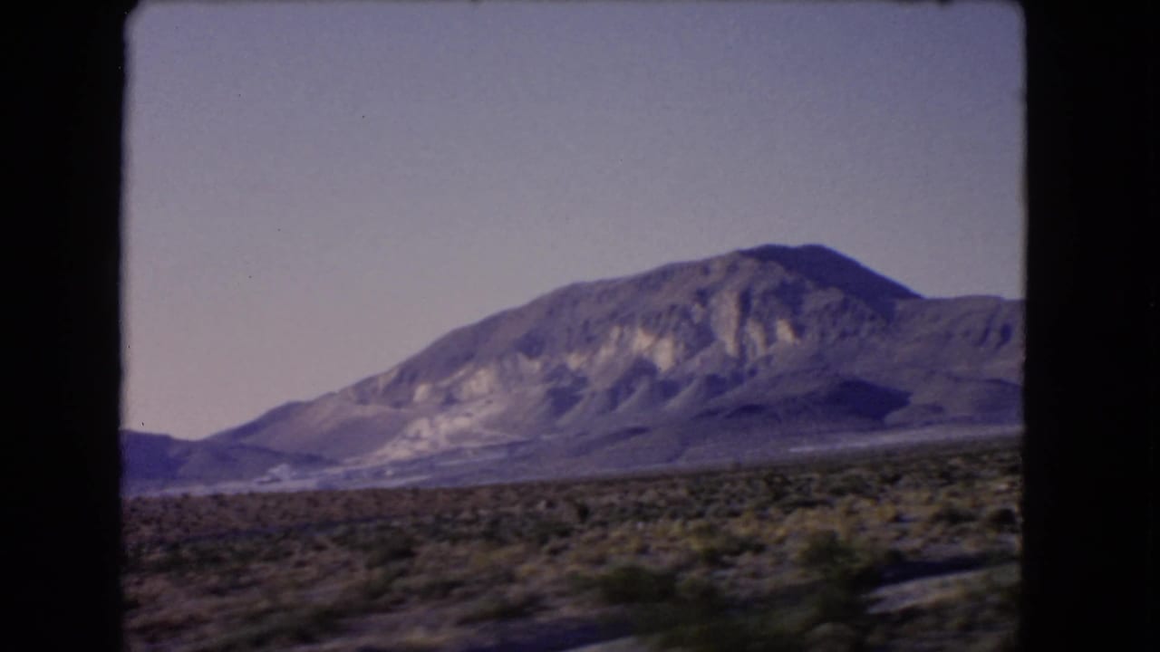 1966 Nevada road footage showing rocky mountains and arid scrubland under a pale sky, with the 8mm frame edge visible.