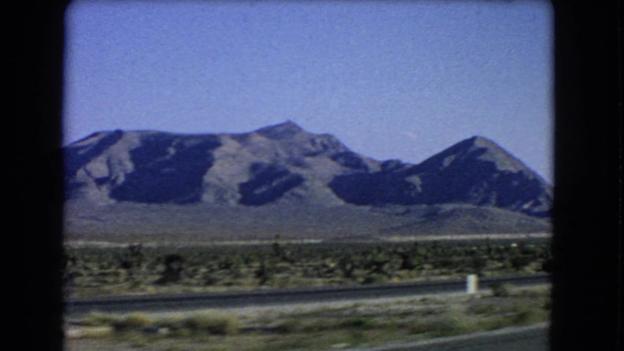 A clear 1966 8mm travel frame shows an open desert road, low scrub, and rugged mountains near Las Vegas, Nevada.