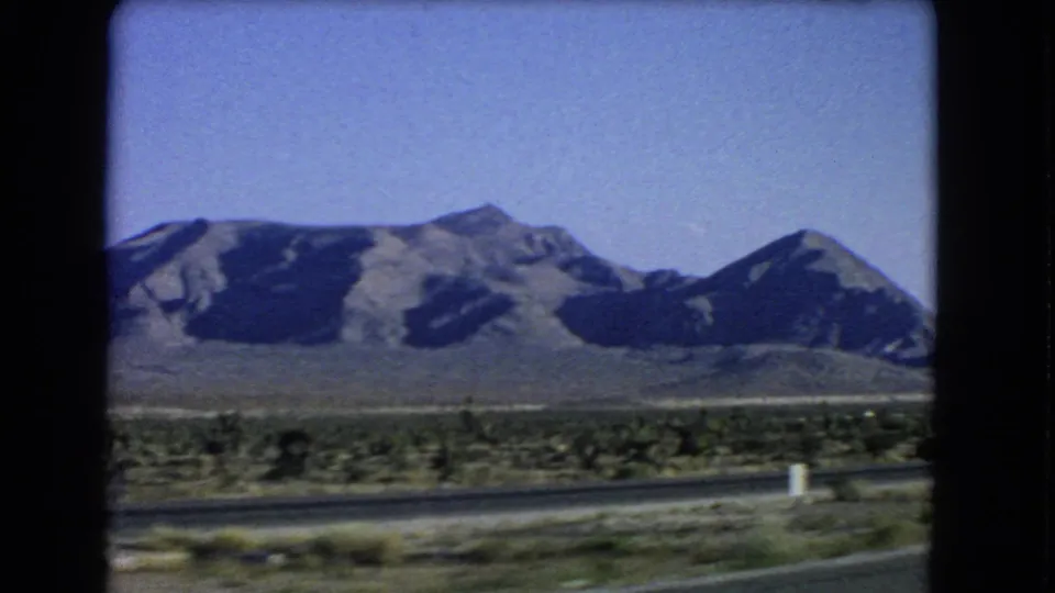 A clear 1966 8mm travel frame shows an open desert road, low scrub, and rugged mountains near Las Vegas, Nevada.