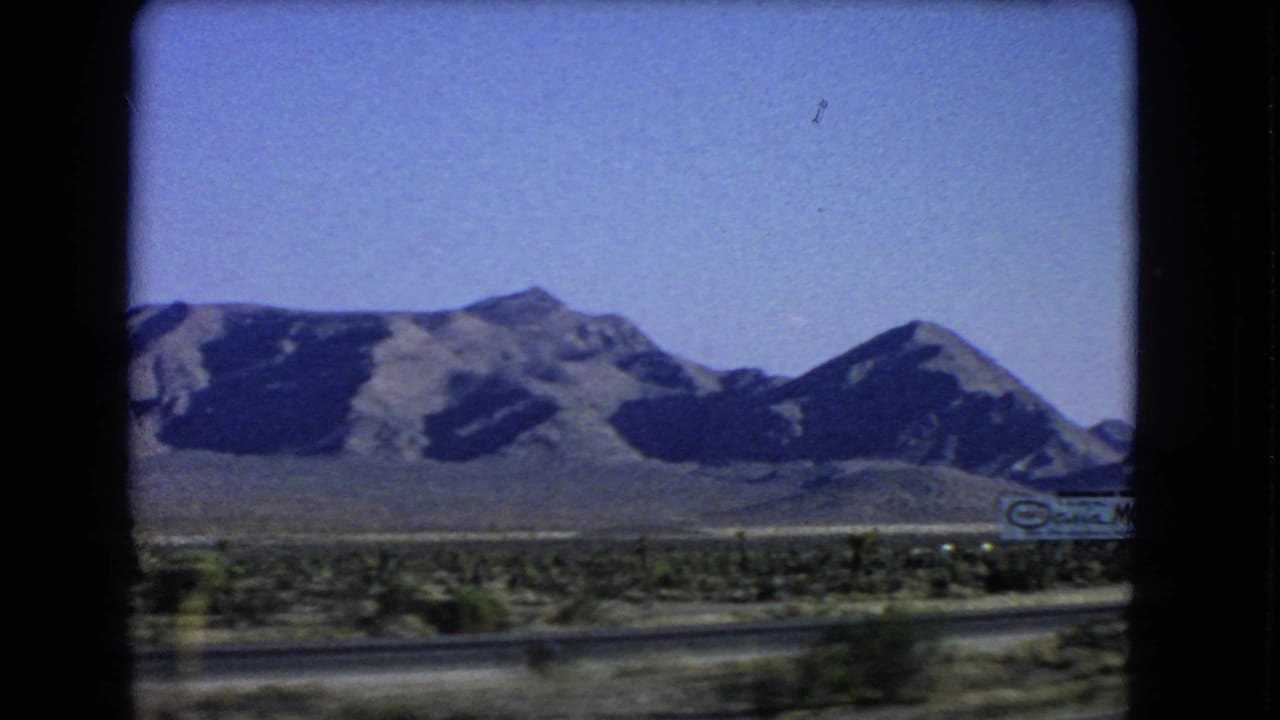 Mountain range beyond desert roadside with a partial roadside sign at right.
