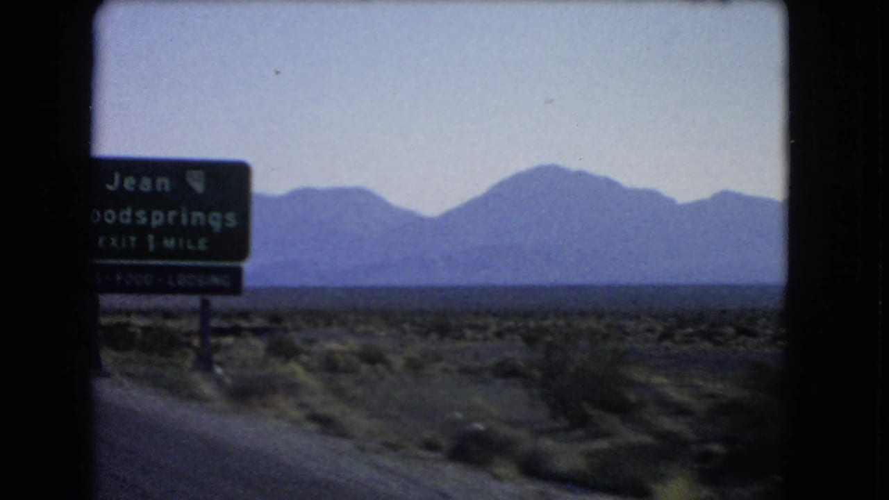 1966 Nevada road-trip frame with a green Jean and Goodsprings exit sign, desert roadside, distant mountains, and open sky.