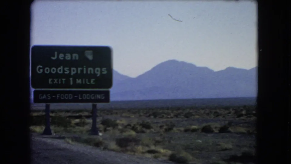 1966 Nevada road-trip frame showing a Jean and Goodsprings exit sign near desert scrub with mountains in the distance.