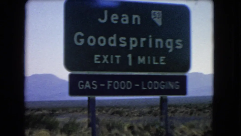 Closer 1966 Nevada view of the Jean and Goodsprings exit sign advertising gas, food, and lodging in a desert setting.