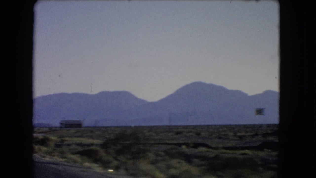 Desert roadside and distant mountains seen from a moving vehicle.