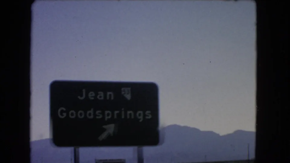 Close 1966 roadside view of the Jean and Goodsprings sign, softened by 8mm focus with desert mountains in the background.